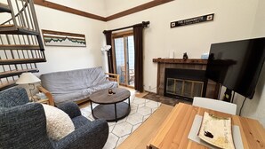 A living room with a sofa, armchair, coffee table, fireplace, TV, and a sign indicating the location.