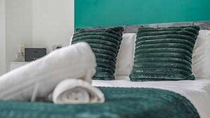A neatly made bed with a green blanket and pillows, a white headboard, and a teal accent wall.