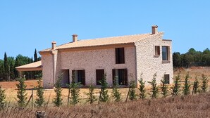A stone house with a tiled roof, multiple windows, and a fenced yard with young trees.