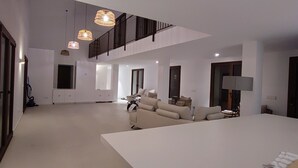 A spacious living area with a large white sofa, a dining table, and a staircase leading to an upper level.