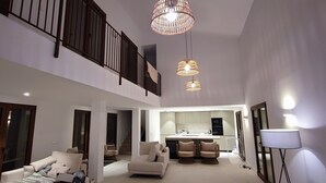 A spacious living area with a high ceiling, a kitchen with modern appliances, and a dining area with two chairs.