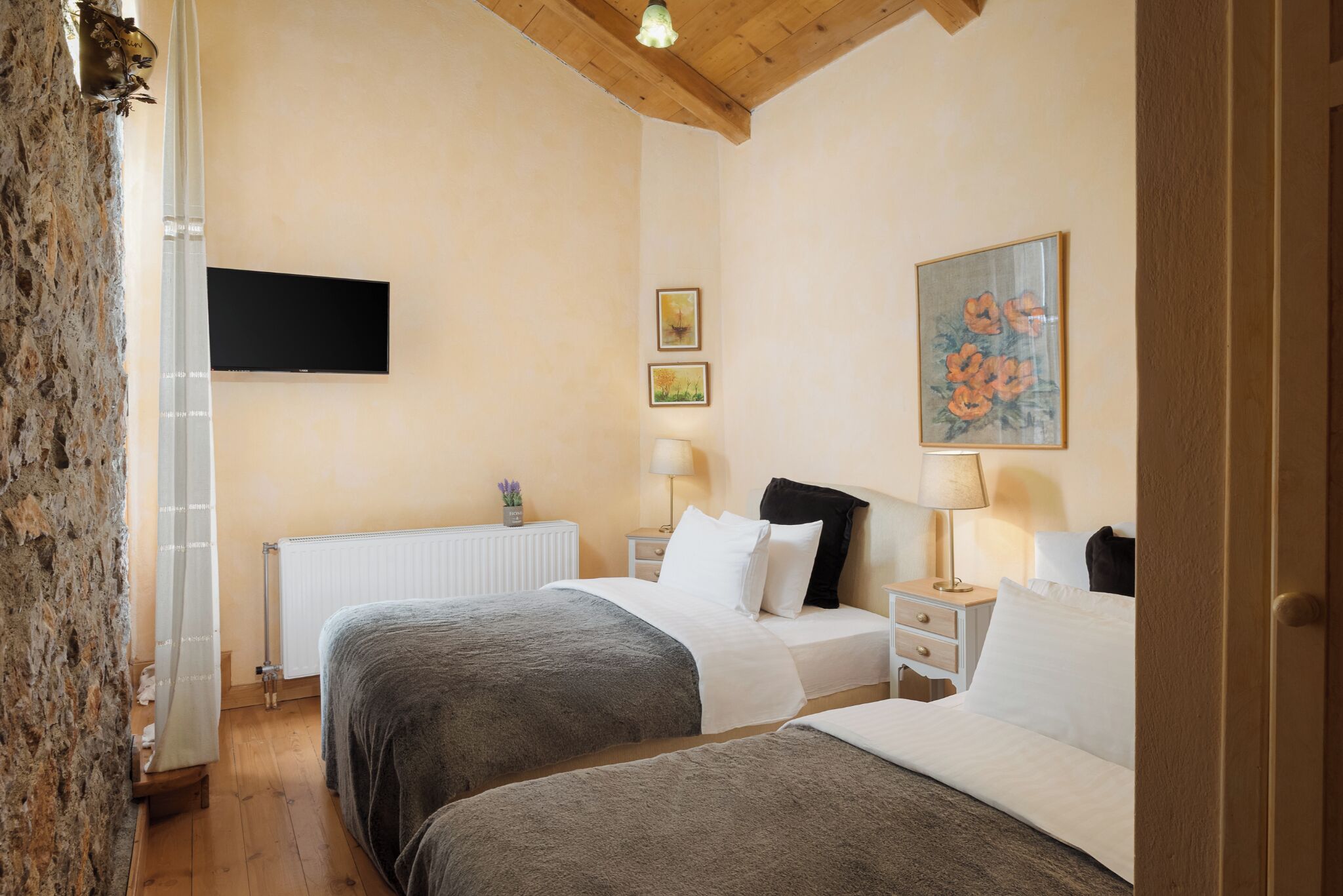 Een slaapkamer met twee bedden, een aan de muur bevestigde televisie en een schilderij.