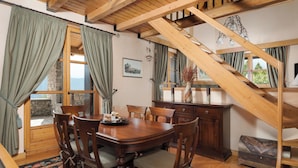 A dining area with a wooden table and chairs, a staircase, and a view of the outdoors.