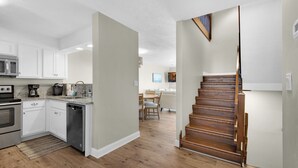 A modern kitchen with white cabinets, a dishwasher, and a wooden staircase leading to a dining area.