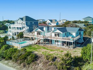 A large, multi-story beachfront property with a swimming pool, multiple decks, and a covered patio area.