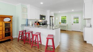 A spacious kitchen with a central island, white cabinetry, and a wooden bar seating area. - Spectacular views from this 2nd Row East side Duplex - New for 2025 Shared Pool (Emerald Isle)