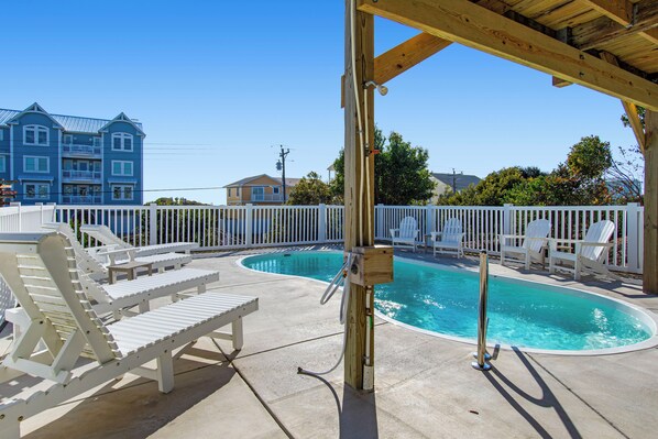 A pool area with white lounge chairs and a wooden deck.