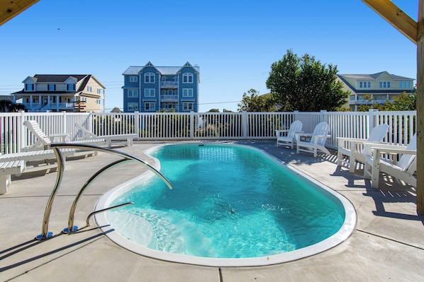 A swimming pool with a white deck, lounge chairs, and a wooden pergola.