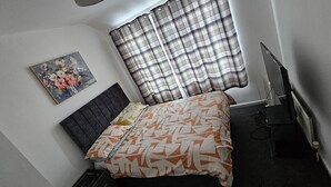 A small, neatly arranged bedroom with a bed, a television, and a painting on the wall. - Cozy 3-bed House in Dagenham (Dagenham)