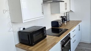 A modern kitchen with white cabinets, a wooden countertop, a microwave, a toaster, and an oven. - Cozy 3-bed House in Dagenham (Dagenham)