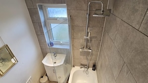 A bathroom with a bathtub, a shower, a sink, and a window. - Cozy 3-bed House in Dagenham (Dagenham)