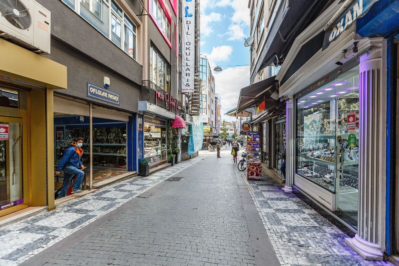 A narrow street lined with shops, including a jewelry store with glass display cases.