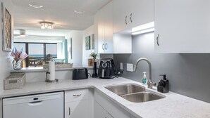 A modern kitchen with white cabinets, a double sink, and a coffee maker. - Sound of the Sea West 115 - Almost Oceanfront 2 BR 2 BA Condo (Emerald Isle)