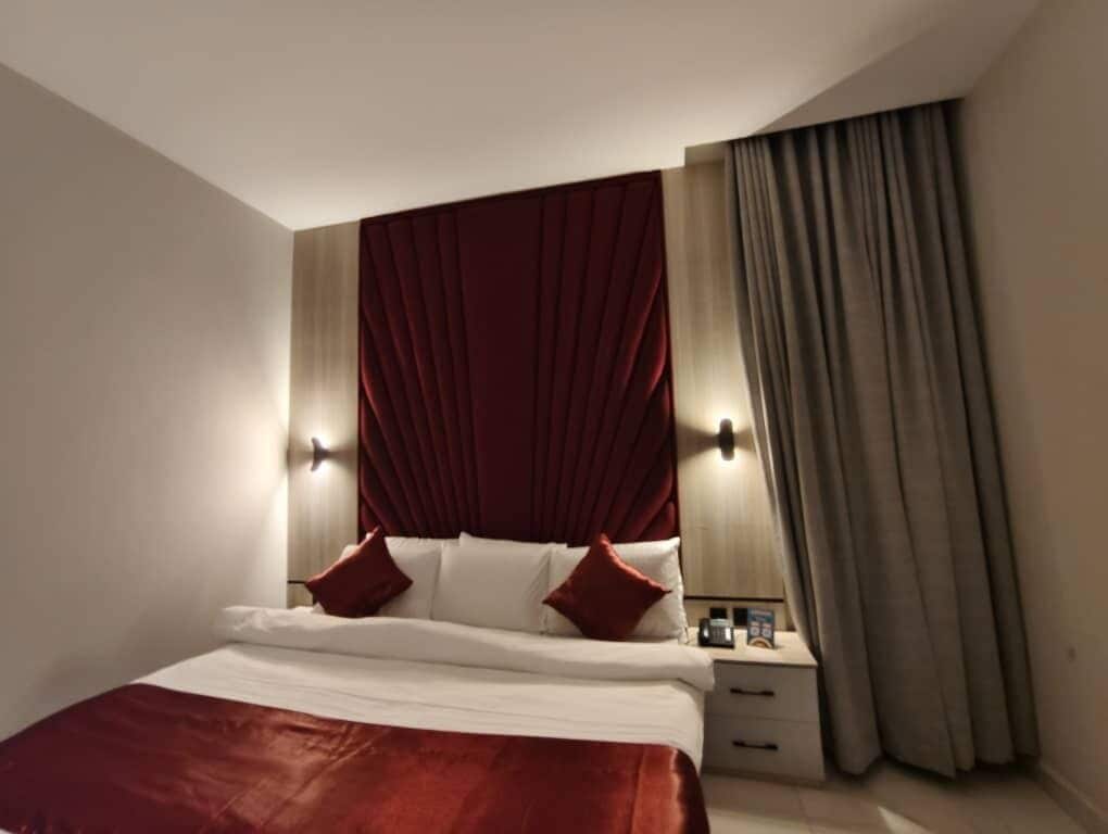 A hotel room with a large bed, a nightstand, a lamp, and a window with curtains.