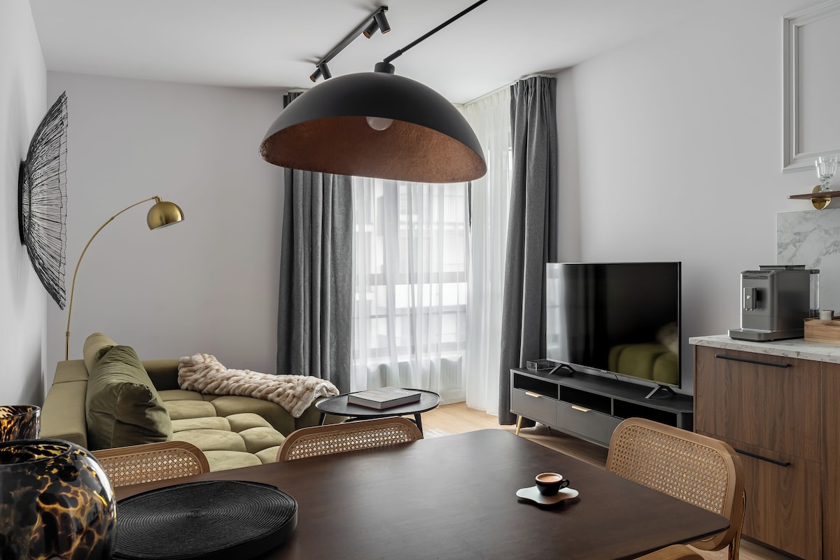 A modern living room with a sofa, a dining table, a TV, and a kitchen area.