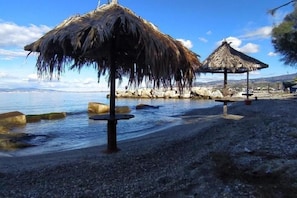Uma praia com guarda-sóis de palha e um trecho de costa rochosa.