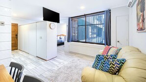 Un salon moderne avec un canapé, un téléviseur fixé au mur et une grande fenêtre avec des rideaux.