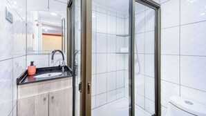 Une salle de bain moderne avec une douche à parois de verre, un lavabo doté d’un plan de travail noir et un meuble en bois.