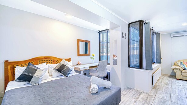 Une chambre à coucher comprenant un lit, un bureau, une chaise, une fenêtre avec des rideaux et un canapé.