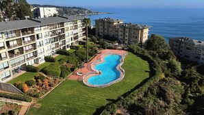 Un hotel de varios pisos con piscina, rodeado de vegetación y vistas a un cuerpo de agua.