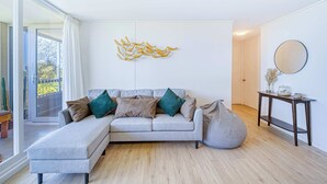 Una sala de estar moderna con un sofá seccional gris, un sillón informal, un espejo redondo y una obra de arte en la pared.