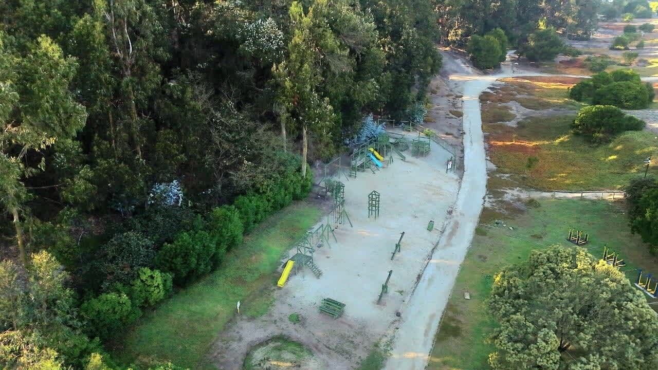 Vue aérienne d’un parc avec des jeux pour enfants, des arbres et un sentier de terre.