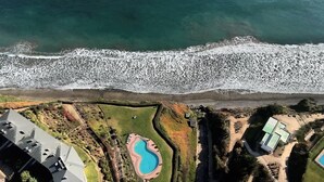 Vista aérea de una propiedad costera con piscina, jardín ajardinado y playa.