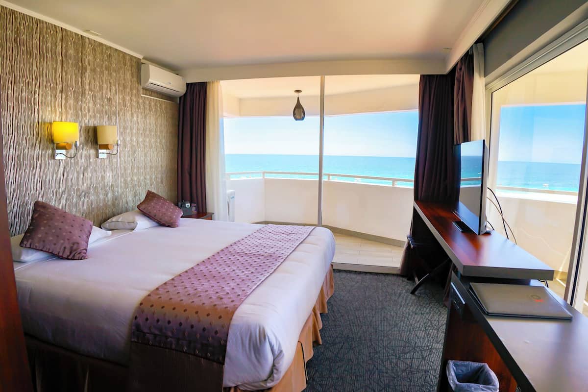 A hotel room with a large bed, a desk with a laptop, a TV, and a view of the ocean.