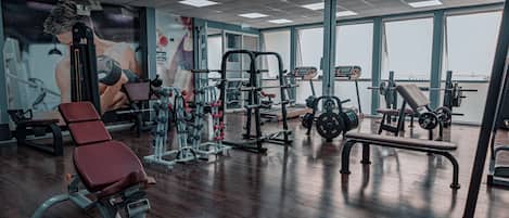 A gym with various exercise equipment, a large mural, and a view of the city through large windows.