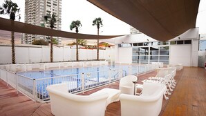 A rooftop pool area with white lounge chairs and a swimming pool.