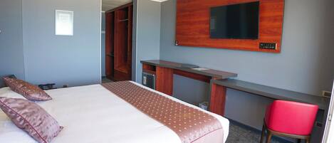 A hotel room with a bed, a desk, a chair, and a TV mounted on the wall.
