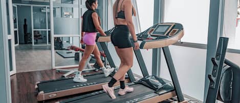 Two people walking on treadmills in a gym with a large window and a mirror.