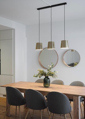 Un coin repas moderne avec une table en bois, quatre chaises et deux lampes suspendues. Deux miroirs ronds sont accrochés au mur, au-dessus de la table.