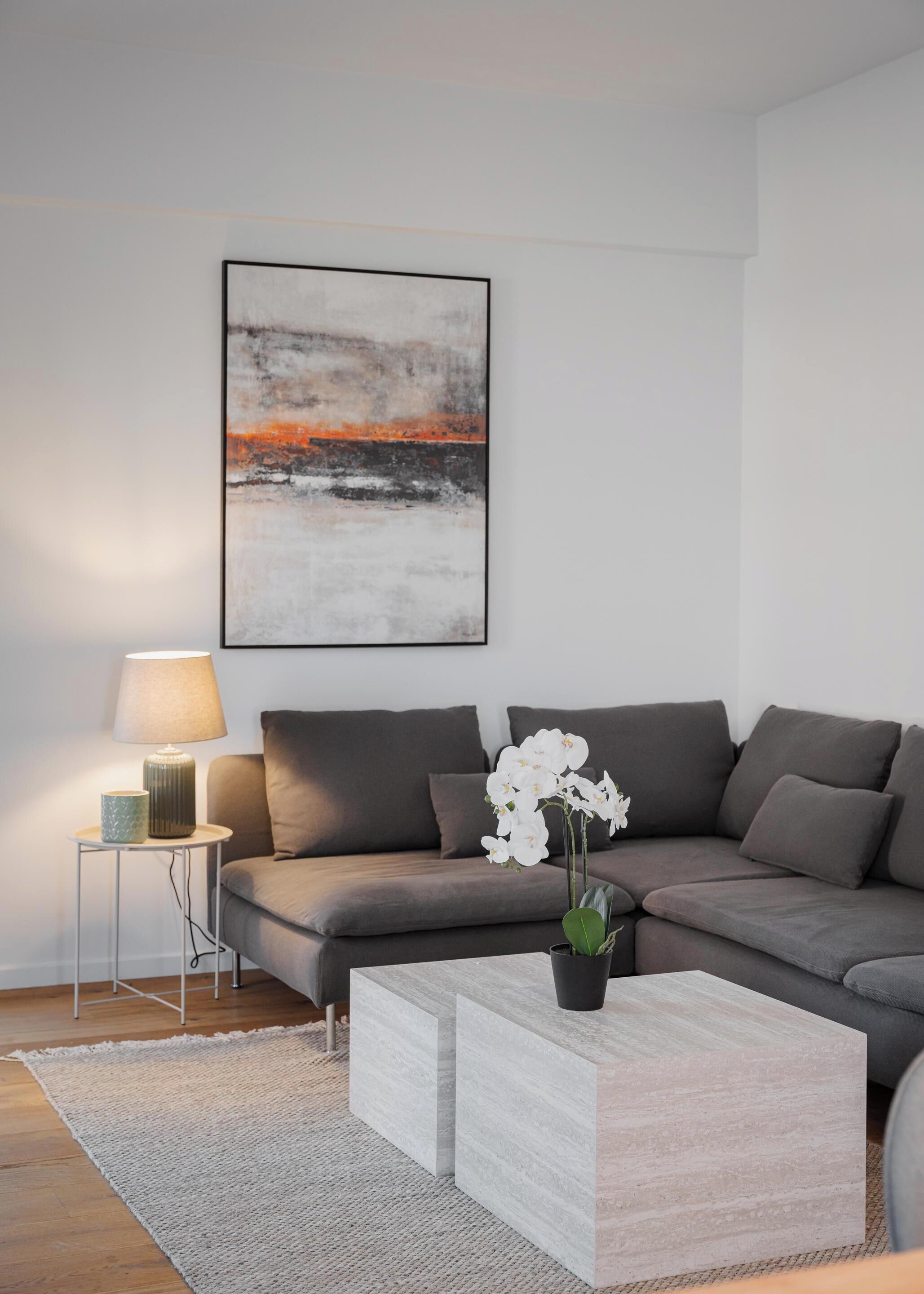 A modern living room with a grey sofa, a coffee table, a lamp, and a framed abstract painting.