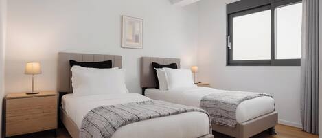 A hotel room with two beds, a nightstand with a lamp, a framed picture on the wall, and a window with curtains.