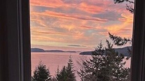 A window with a view of a sunset over a body of water, surrounded by trees.