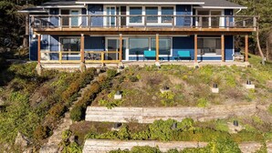 A two-story house with a balcony, large windows, and a view of the surrounding forest.