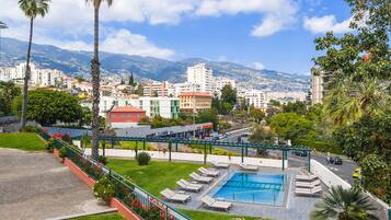 Un hotel con piscina, sillones de descanso y vistas a la ciudad y las montañas.