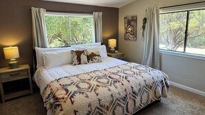 Een slaapkamer met een groot bed, twee nachtkastjes met lampen, een raam met gordijnen en een wand met decoratie.