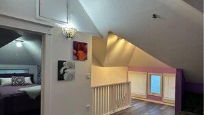 Amplio dormitorio tipo loft con techo inclinado, una cama, un rincón de descanso y una escalera que conduce a un nivel superior.