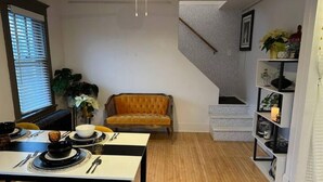 Un área de comedor con una mesa preparada para dos, un sofá y una escalera que sube a otro nivel.