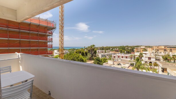 A balcony with a white table and chairs, a view of a cityscape, and a construction crane in the background. - Sea View Apartment Ac Gallipoli (Gallipoli)