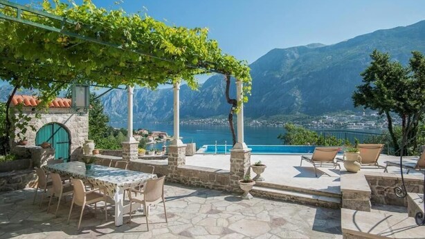 A terrace with stone flooring, outdoor seating, and a view of a mountain and sea.