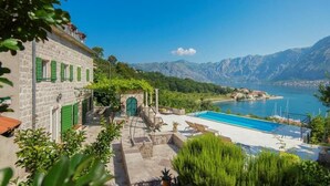 A stone building with a pool, surrounded by greenery and mountains.