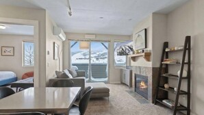 A modern room with a fireplace, a dining area, and a view of snowy mountains through large windows.