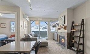 Una habitación moderna con chimenea, zona de comedor y vistas a montañas nevadas a través de amplios ventanales.