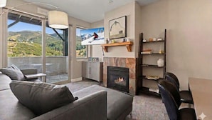 A modern living room with a sofa, a fireplace, a television, and a view of a mountainous landscape through large windows.
