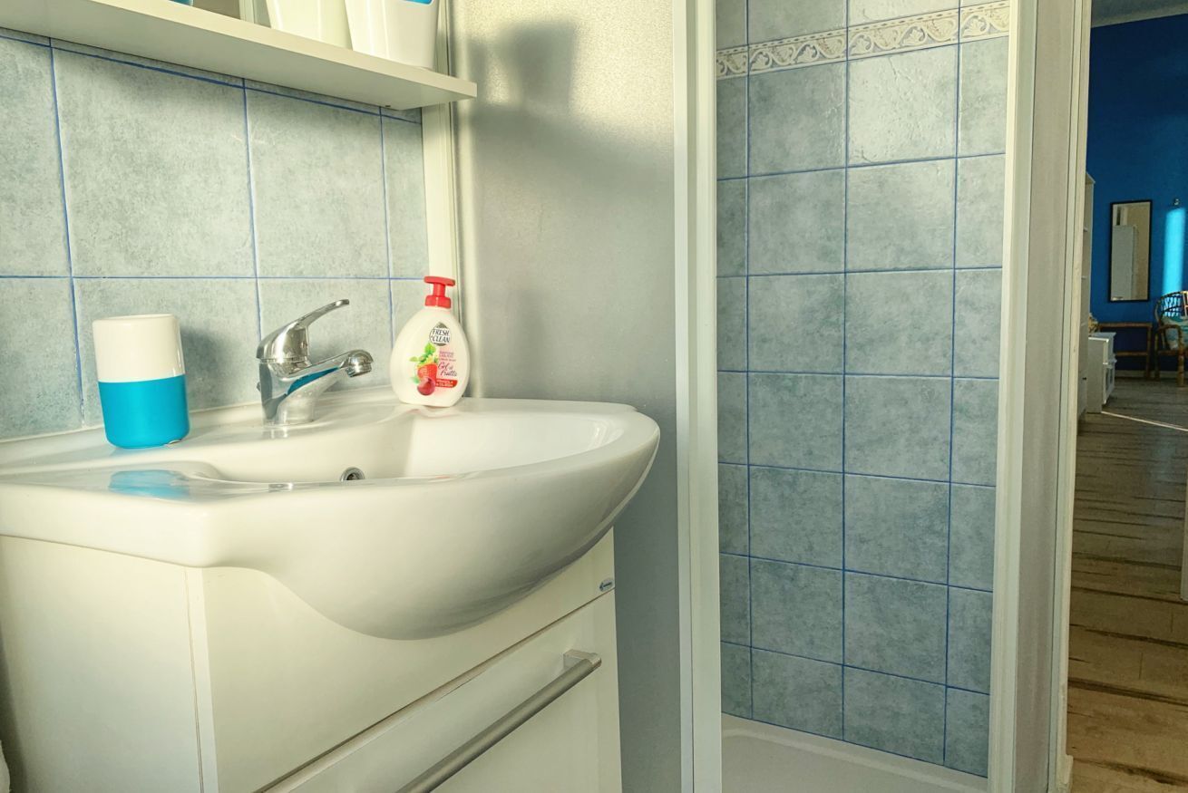 A bathroom with a white sink, blue tiles, a white cup, and a bottle of hand soap.