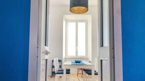 Une pièce avec une table blanche, des chaises bleues, une fenêtre et un luminaire suspendu.