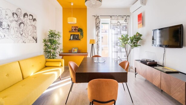 A modern living space with a yellow sofa, a dining table, and a TV mounted on the wall. - HOUSE OF MUSIC in Pigneto, METRO C to Colosseo (Roma)